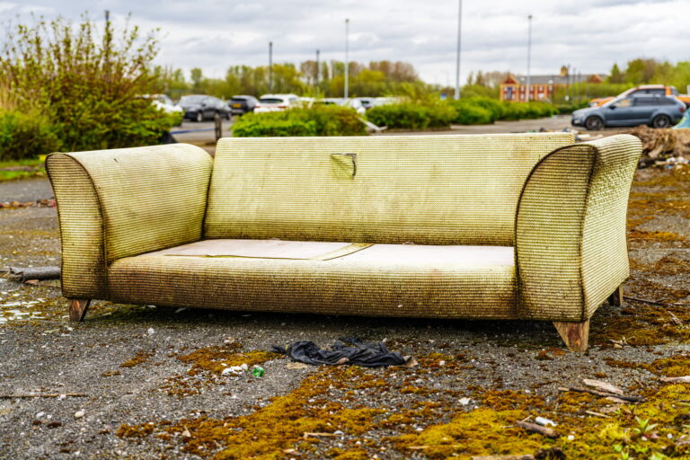 Fly tipping, rubbish dumped illegally by the road side. Large sofa.